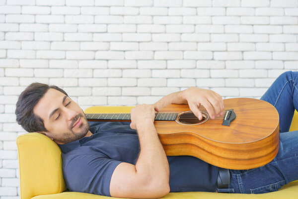 Happy man playing guitar while sitting on sofa in living room, Enjoying carefree time at home.