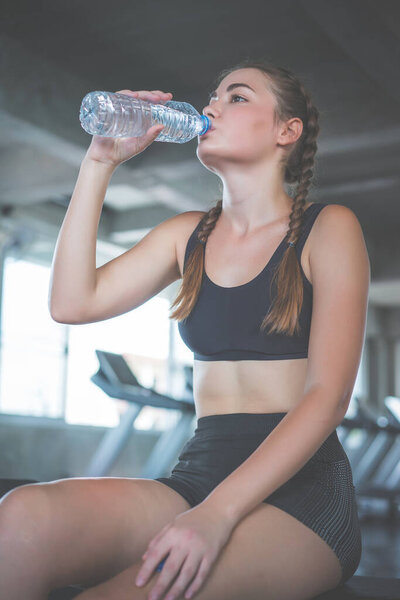 Beautiful young woman drinks water in gym. Sports nutrition concept.