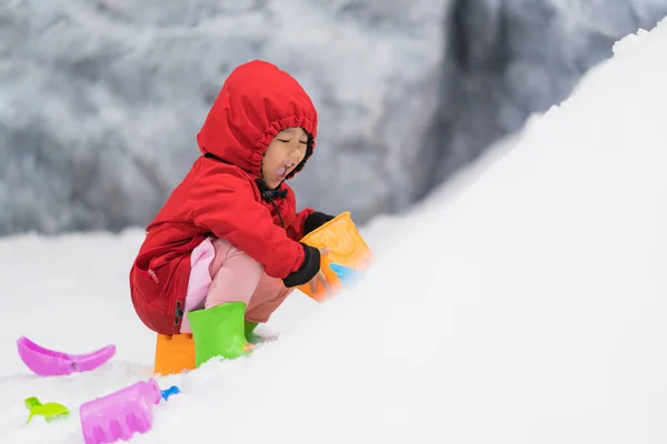 Child playing with snow in winter. Little Child in colorful jacket and knitted hat playing with snow in winter park on Christmas.