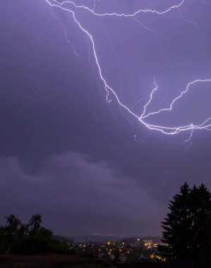 mavi gökyüzü ile gece boyunca bir ağaç ile bir şehir üzerinde yıldırımlar