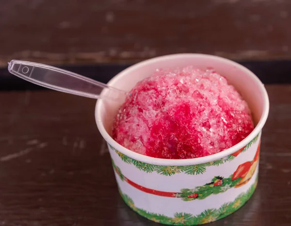 shaved ice with strawberry syrup in small bowl on wooden table.