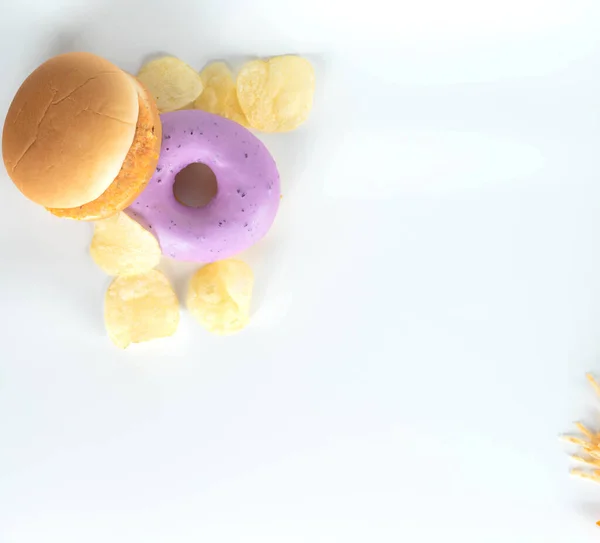 junk food dish such as donut,potato chips, burger, fish fingers on white background,in top view with copy space
