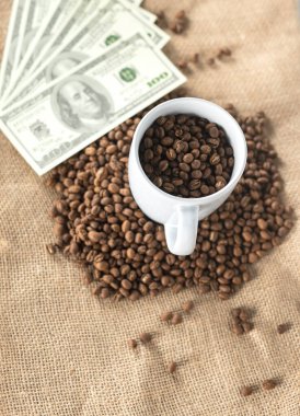Kahve fincanındaki kahve çekirdekleri bir yığın kahve çekirdeği ve bir dolarlık banknot. Kahve ticareti konsepti. kahve çekirdeği ekonomisi.