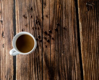Kahve fincanı ve kahve çekirdekleri yukarıdan bakıldığında ahşap bir arka planda duruyordu.