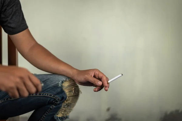 男人坐在椅子上 手里拿着一支香烟 因为他在墙上抽烟 毒品的概念 — 图库照片