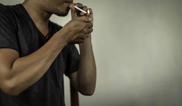 man holds a burning cigarette behind the wall. concept for drug,illness, crime.