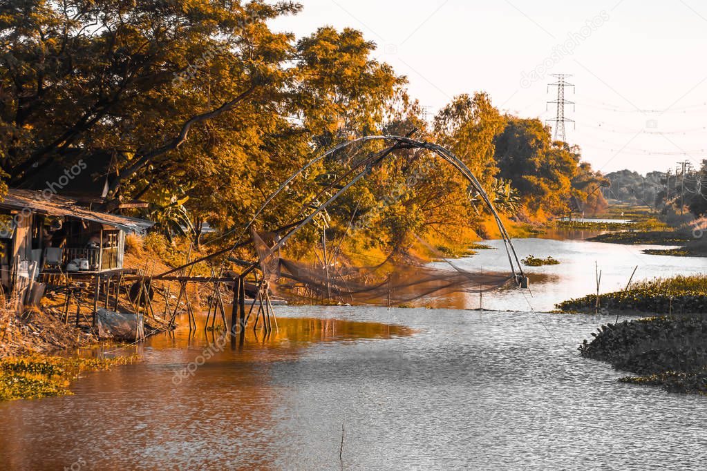 A traditional wooden t  fishing trap with a golden orange beautiful forest along river in Thailand  background