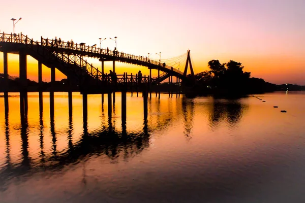 Menschen Silhouetten beobachten bunten Sonnenuntergang Brücke Sonnenuntergang Flussbrücke Menschen Silhouette bewundern Tapeten Silhouetten von Menschen zu Fuß über die ikonische Brücke über den Fluss bei Sonnenuntergang — Stockfoto