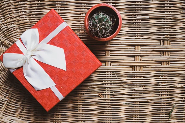 gift red box with white ribbonon woven bamboo wood background cozy and warm home welcome concept ide and small lovely green cactus