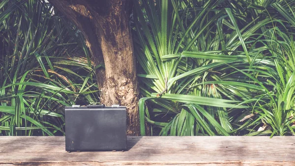 緑の自然の背景を持つ木製の表面に黒いビジネスレザーブリーフケース — ストック写真