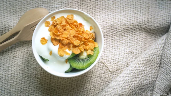 Corn flakes, cereal and milk splash in bowl. Natural homemade plain organic yogurt in wood bowl on wood texture background