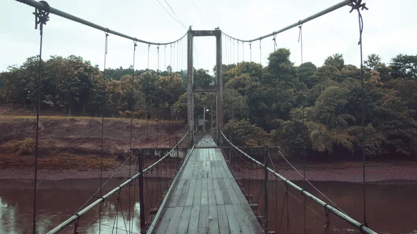 Suspension structure bridge over the river. Wooden construction floor suspension bridge