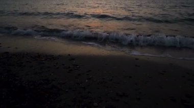 Yunanistan'da akşam geç saatlerde kırmızı gün batımı sırasında sahilde çöken kırmızı dalgaların yakın görünümü
