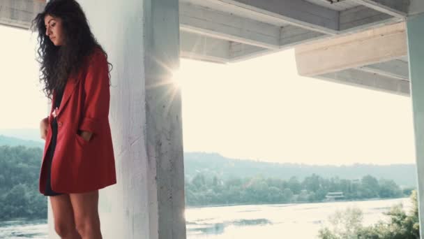 Modelo feminino morena encantadora com casaco vermelho e vestido preto posando contra o sol — Vídeo de Stock