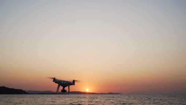 Drone negro con cámara digital volando sobre la superficie del mar y disparando el atardecer — Vídeo de stock