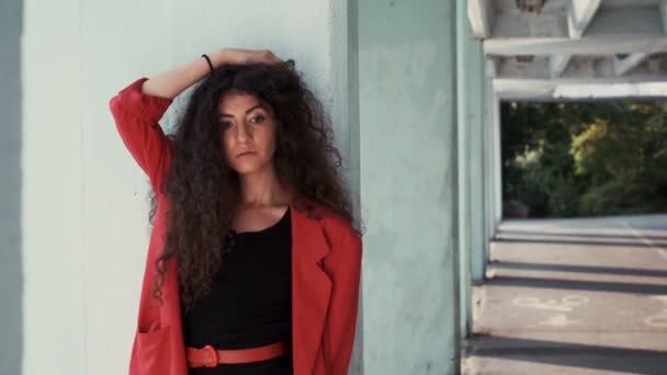 Mujer de moda en vestido negro y chaqueta roja jugando con su pelo — Vídeos de Stock