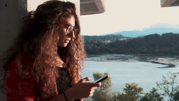 Молода дівчина в окулярах смс на смартфоні і посміхається — стокове відео