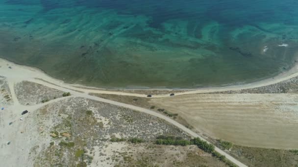 Largo tiro de coches conduciendo lento en camino de playa cerca de aguas turquesas tranquilas en Lemnos, Grecia — Vídeo de stock