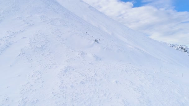 Воздушный беспилотник с видом на зимний горный ландшафт и группу лыжников, спускающихся по склону — стоковое видео