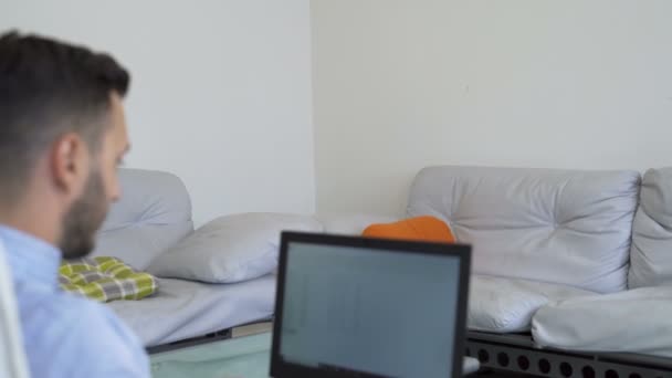 Jeune homme d'affaires barbu est assis à la table dans le bureau à la maison en face de l'ordinateur portable et l'écriture dans un ordinateur portable . — Video