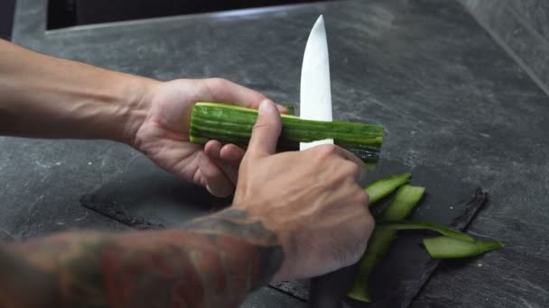 긴 칼로 신선한 오이를 벗겨 문신으로 남성의 손을 닫습니다. — 비디오