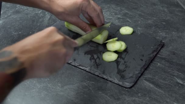 Primer plano en las manos masculinas corte fresco, pepino verde en tablero de piedra y hacer ensalada . — Vídeos de Stock