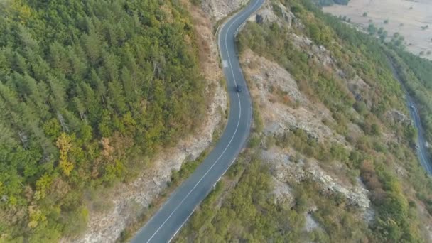 Беспилотник, гоняющийся за автомобилем по извилистой дороге через зеленый лес на горном склоне — стоковое видео