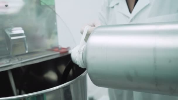 Scientist in white clothes and gloves filling big container with black CBD hemp oil — Stock Video