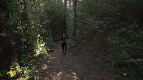 Vista frontal, imágenes en cámara lenta de ajuste, mujer joven con pelo largo marrón sendero corriendo en el bosque por la mañana — Vídeos de Stock