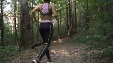 Jimnastik yapan kız ormanda koşuyor ve elinde su şişesi tutuyor.