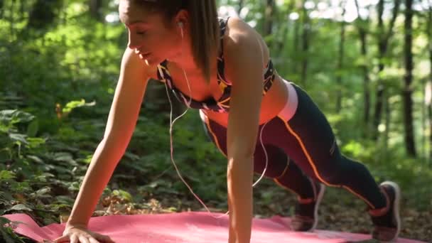 Filmato al rallentatore di una ragazza in forma che fa flessioni e ascolta musica con le cuffie nel parco — Video Stock