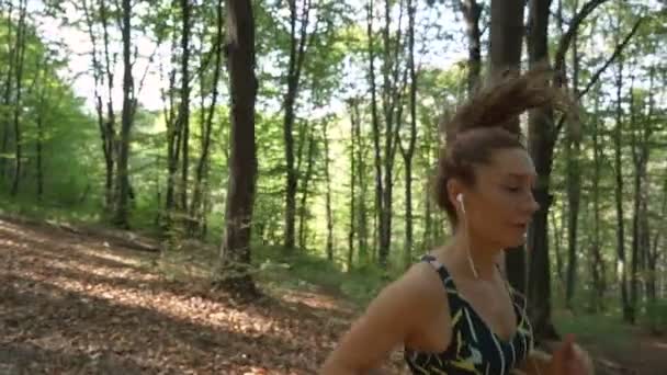 Close view of fit girl listening music and running on hard terrain in forest — Stock video