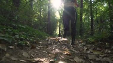 Kaslı, kulaklık takan, orman yamacında koşan, ağaçların arasında parlayan seksi bir kız.