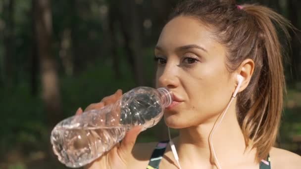 Brunette fitness girl with white headphones drinking water and resting after workout — Stock Video