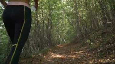 Ormanın derinliklerinde orman yolunda koşarken elinde su şişesi tutan fitness kızının düşük açılı görüntüsü.