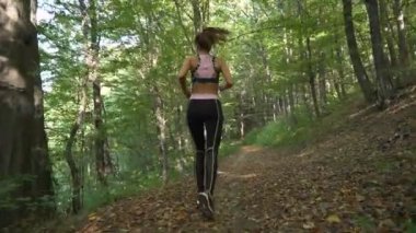 Sonbaharda orman yolunda koşan fitness kızının yavaş çekim kamerası.