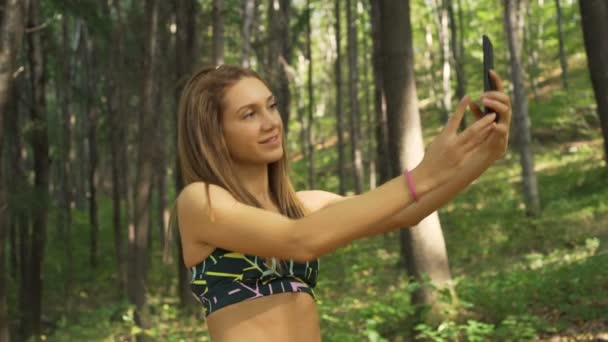 Ragazza attiva con grande corpo e addominali, sorridente durante lo scatto di foto selfie con smartphone all'aperto — Video Stock