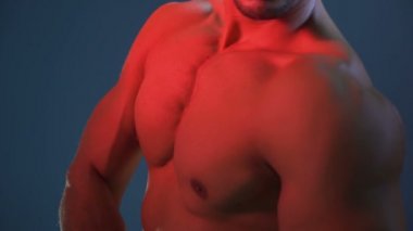 Gömleksiz, yırtık bir adam kolunu açmış, pazılarını ve omuz kaslarını gösteriyor.