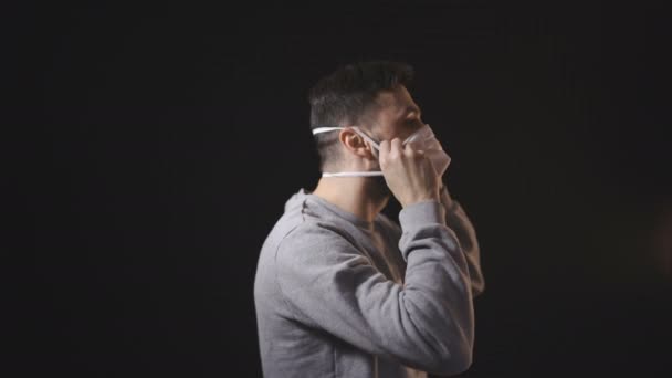 Mann setzt weißen Mundschutz vor schwarzen Hintergrund — Stockvideo