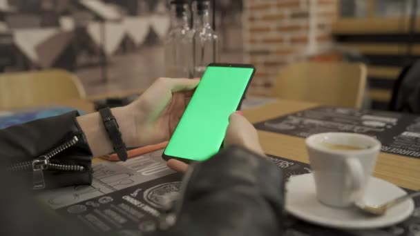 Žena sedí v kavárně s šálkem horké kávy a pomocí smartphone se zelenou obrazovkou — Stock video