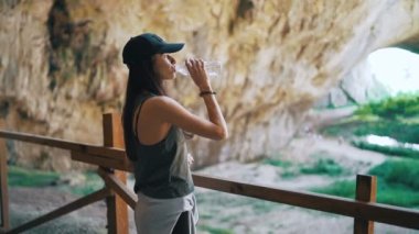 Devetaki mağarasını keşfeden turist kadın bir yudum su içip manzaranın tadını çıkarıyor.
