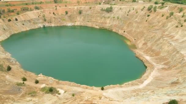 Nerozpoznatelná žena sedící na okraji opuštěné důlní jámy plné vody a fotící
