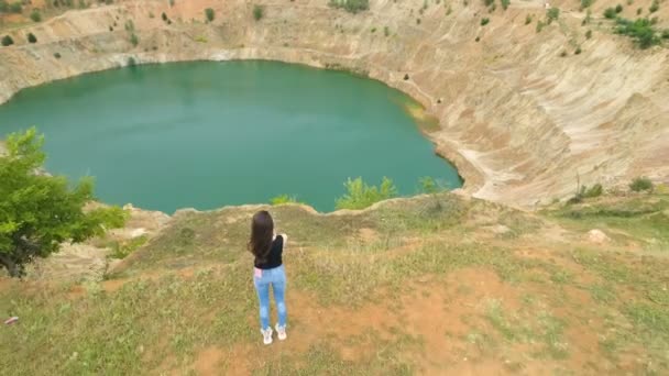 Mujer joven con jeans y cabello castaño largo sentada en el borde de la mina y tomando fotos con la cámara — Vídeos de Stock