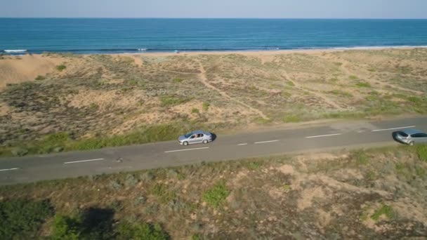 Drone volgt auto langzaam rijden op asfaltweg langs de zeekust met prachtig uitzicht — Stockvideo