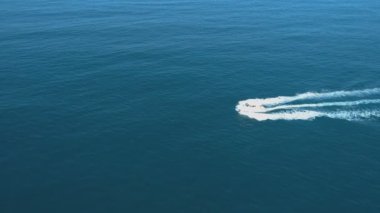 Denizde hızla giden teknenin havadan görünüşü arkasında beyaz bir köpük izi bırakıyor.