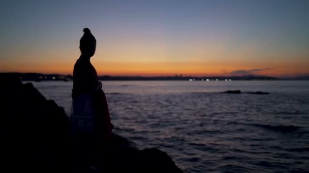 Mujer sentada en la playa mirando el atardecer junto al mar disfrutando de la vista — Vídeos de Stock