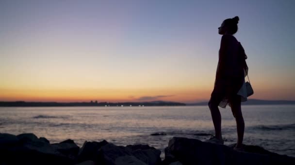 Silueta přemýšlivé osamělé ženy sedící na skále a užívající si krásného západu slunce nad mořem — Stock video