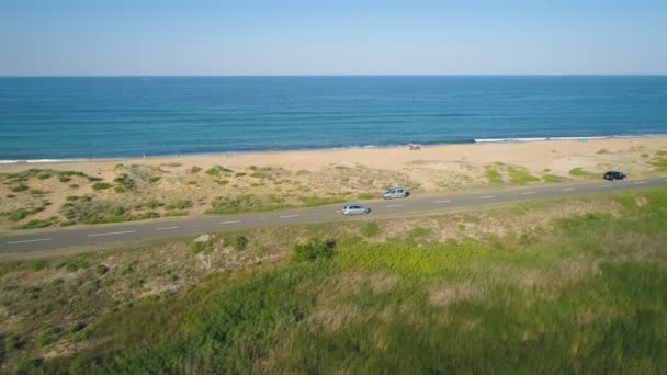 Панорамный вид на автомобили, медленно движущиеся по морской дороге с песчаным пляжем и спокойным морским горизонтом с голубым небом — стоковое видео