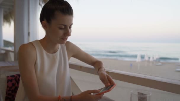 Красива молода жінка насолоджується вечерею в пляжному ресторані з морськими хвилями на пляжі на задньому плані — стокове відео