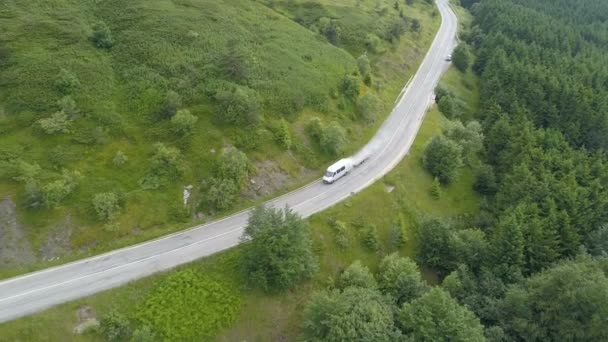 Bílá dopravní dodávka nebo autobus po klikaté horské silnici se zelenými kopci, letecký pohled — Stock video